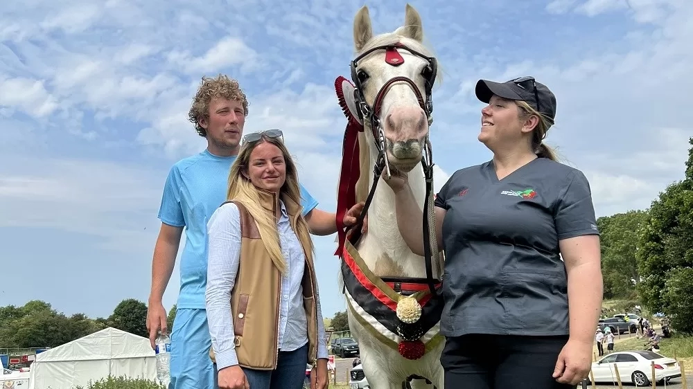 A brown and white pony wearing a winner's sash stands next to Redwings vet Nicola and their owners.