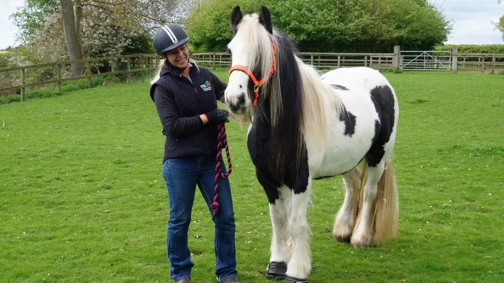 Nursing Manager Louise Gedge stands in a grassy paddock next to black and white pony Audrey.