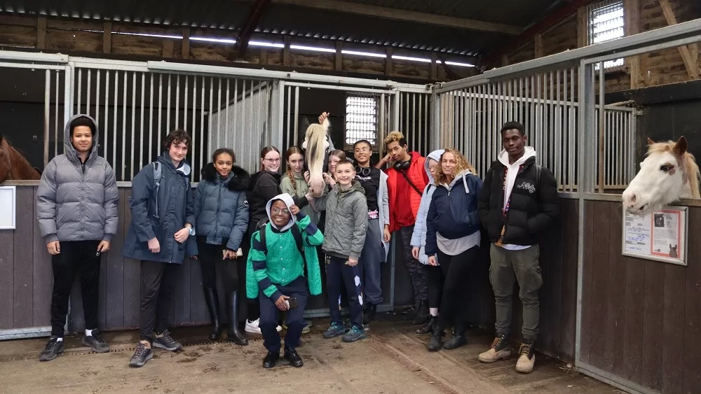 A group of young people gather around a stable door where Harley the pony is standing.