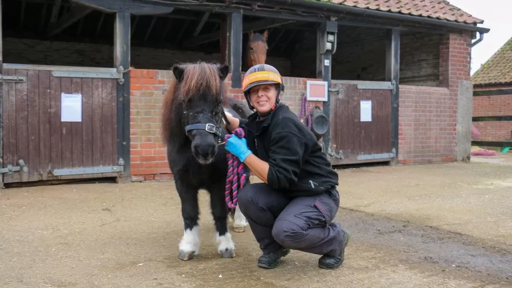 Little Shetland pony Marjorie stands outside some stables with Nursing Manager Lou.