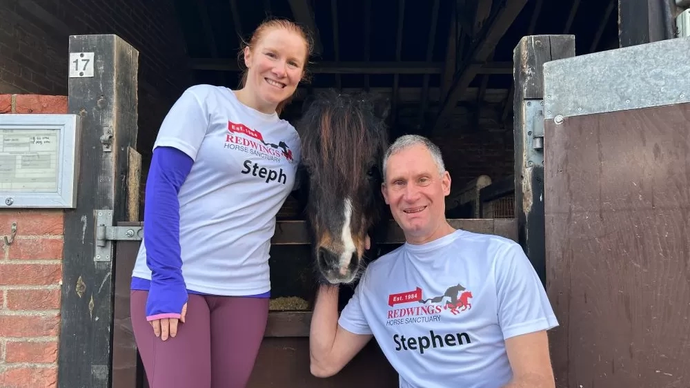 Two supporters in Redwings running tops stand next to a stable with a small pony poking his head over the top.