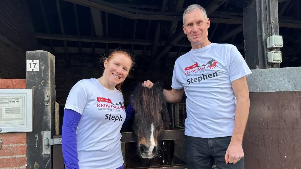 Two supporters wearing Redwings running tops stand outside a stable with a small pony poking their head over the door.