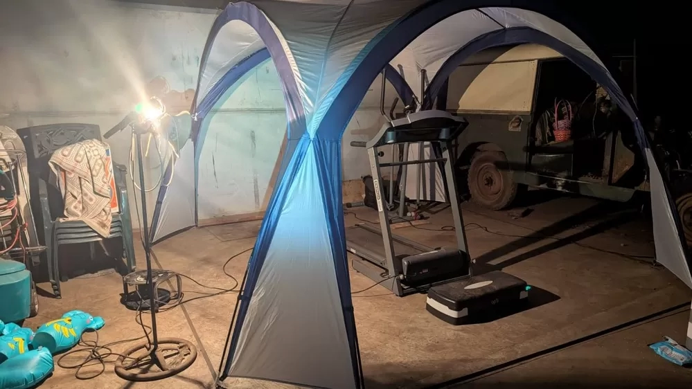 A treadmill is under a gazebo in a farm outbuilding, dimly lit with a lamp