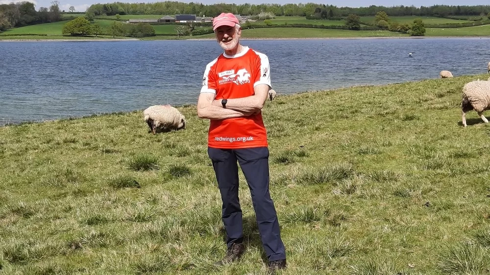 Trustee Ian, wearing a Redwings branded sports shirt, stood in front of a lake and some sheep