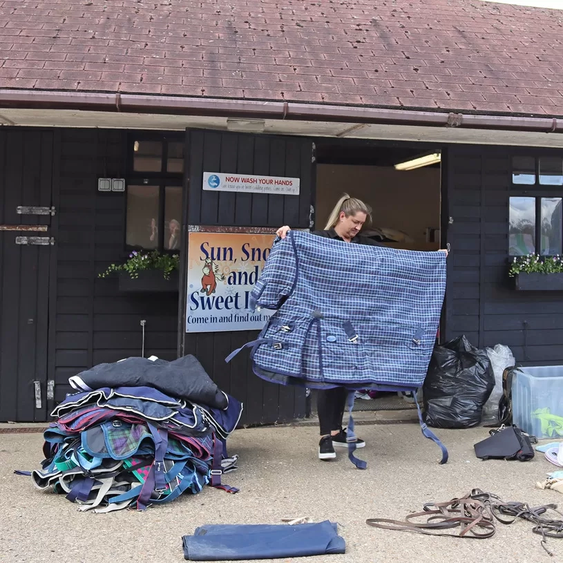 A woman is folding and sorting horse rugs in front of a Redwings building