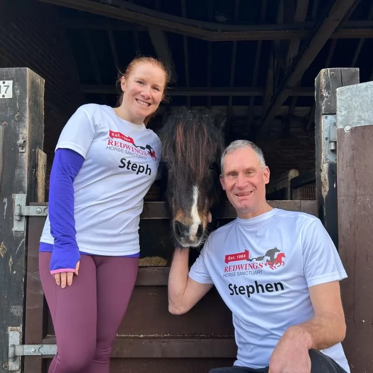 Two supporters in Redwings running tops stand next to a stable with a small pony poking his head over the top.