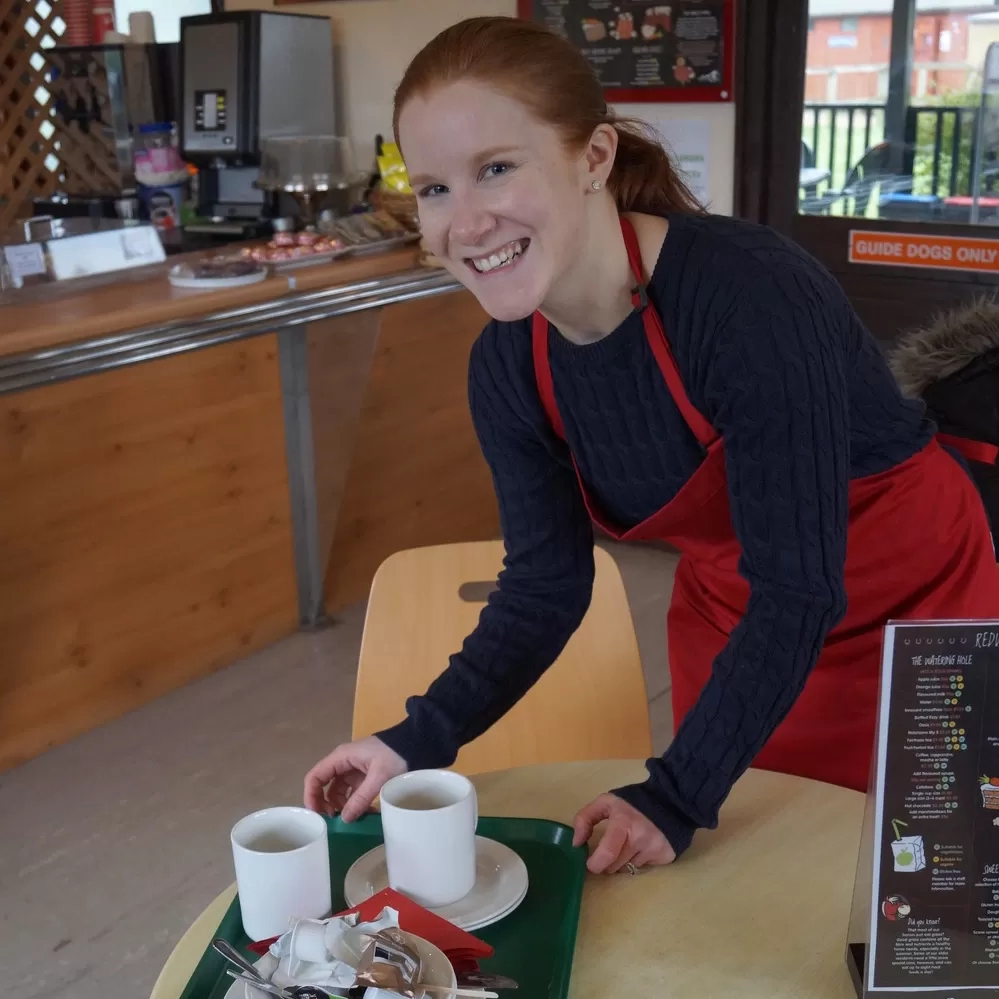 A volunteer is clearing a table in a Redwings café 