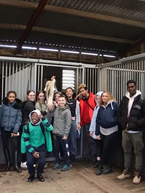 A group of young people gather around a stable door where Harley the pony is standing.