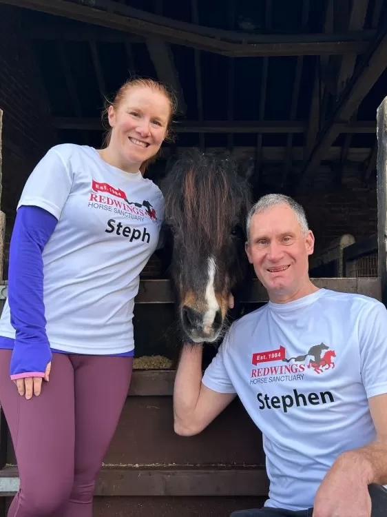 Two supporters in Redwings running tops stand next to a stable with a small pony poking his head over the top.