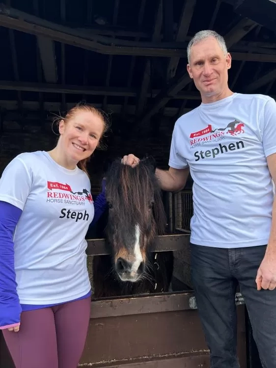 Two supporters wearing Redwings running tops stand outside a stable with a small pony poking their head over the door.