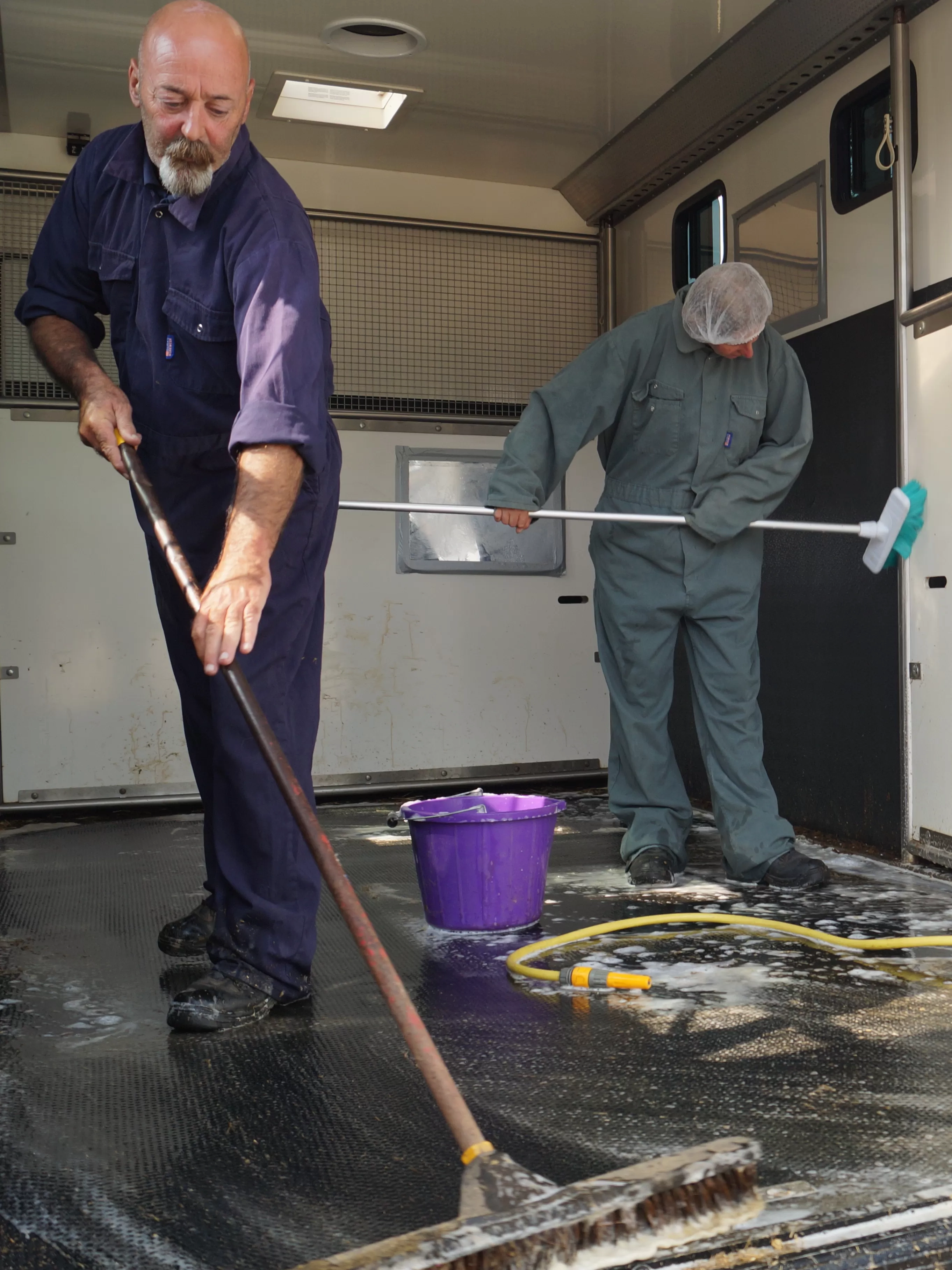 Photo of two people in overalls scrubbing a horsebox